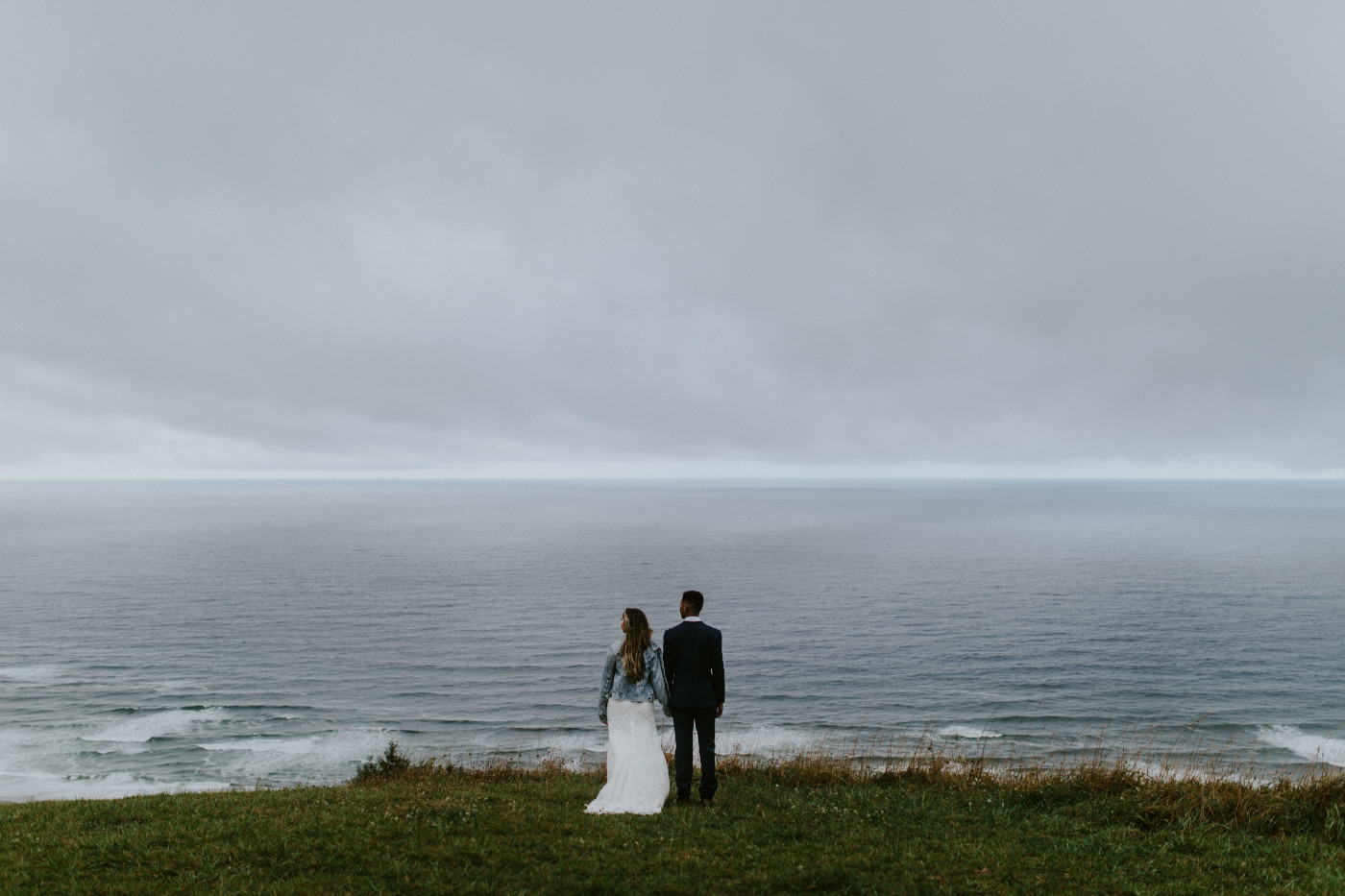 Bride and groom stand side by side near a cliff edge in front of the ocean in Oregon. Elopement photography at Mount Hood by Sienna Plus Josh.