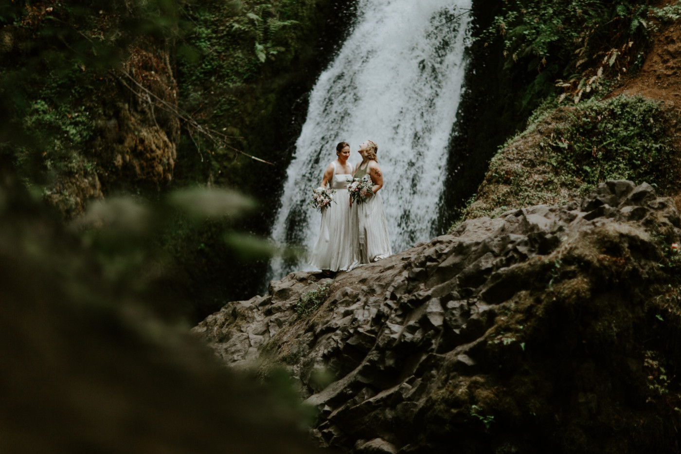 Kate and Audrey stand together in front of Bridal Veil Falls. Elopement wedding photography at Bridal Veil Falls by Sienna Plus Josh.