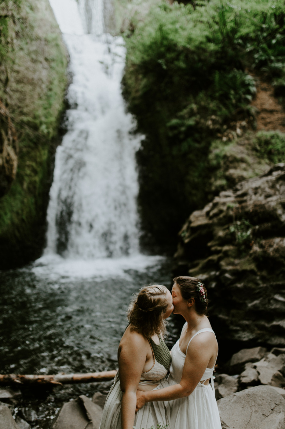 Kate and Audrey kiss in front of a waterfall. Elopement wedding photography at Bridal Veil Falls by Sienna Plus Josh.