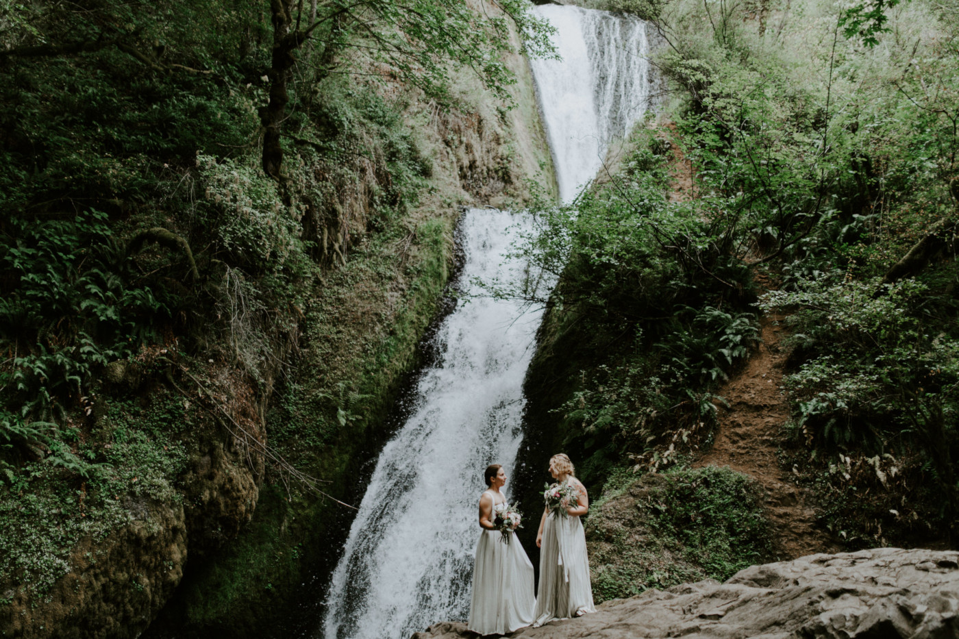 Audrey and Kate stand in front of each other at Bridal Veil Falls. Elopement wedding photography at Bridal Veil Falls by Sienna Plus Josh.