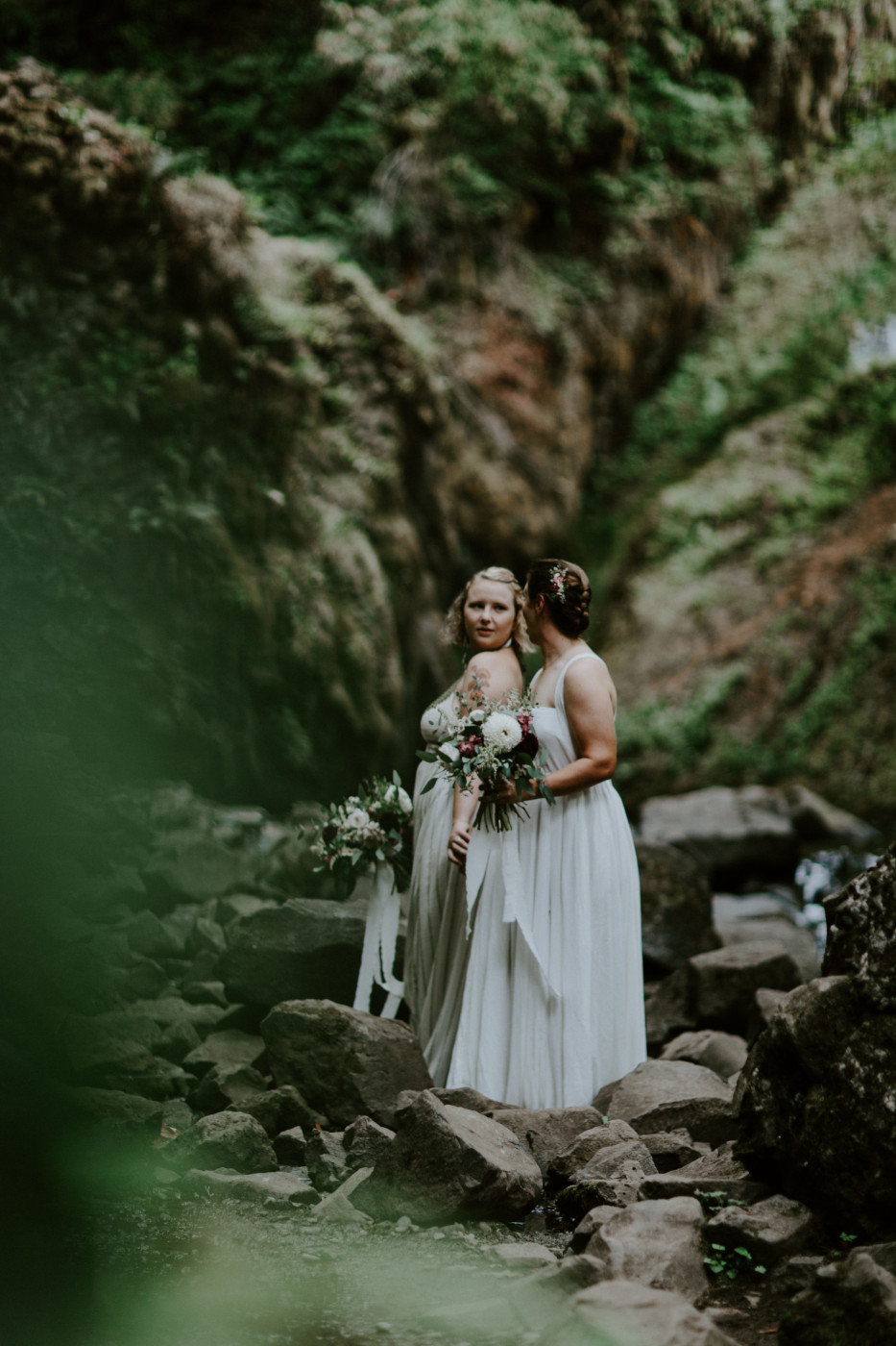 Kate and Audrey stand on the stones along the river. Elopement wedding photography at Bridal Veil Falls by Sienna Plus Josh.