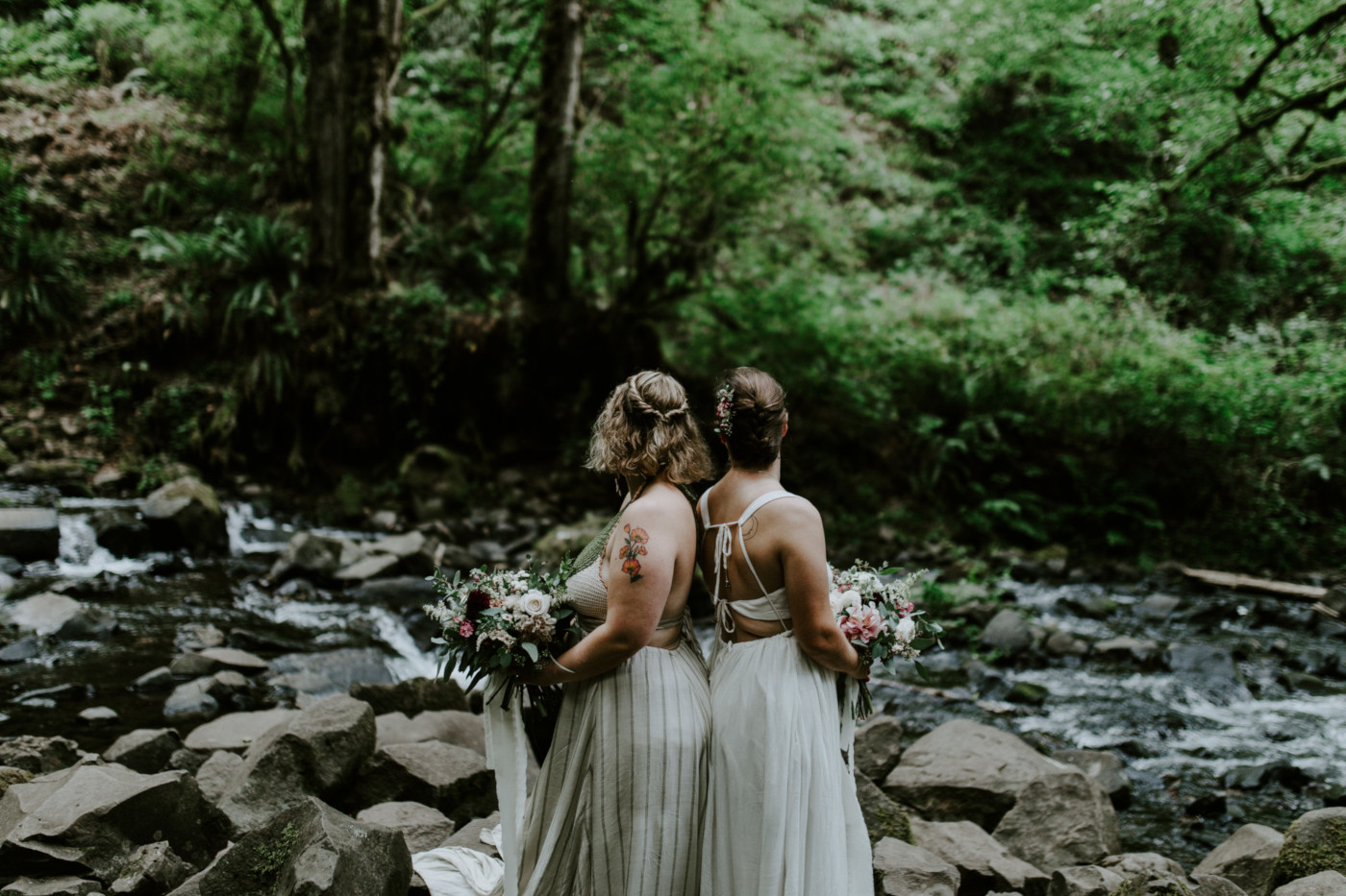 Kate and Audrey stand back to back. Elopement wedding photography at Bridal Veil Falls by Sienna Plus Josh.