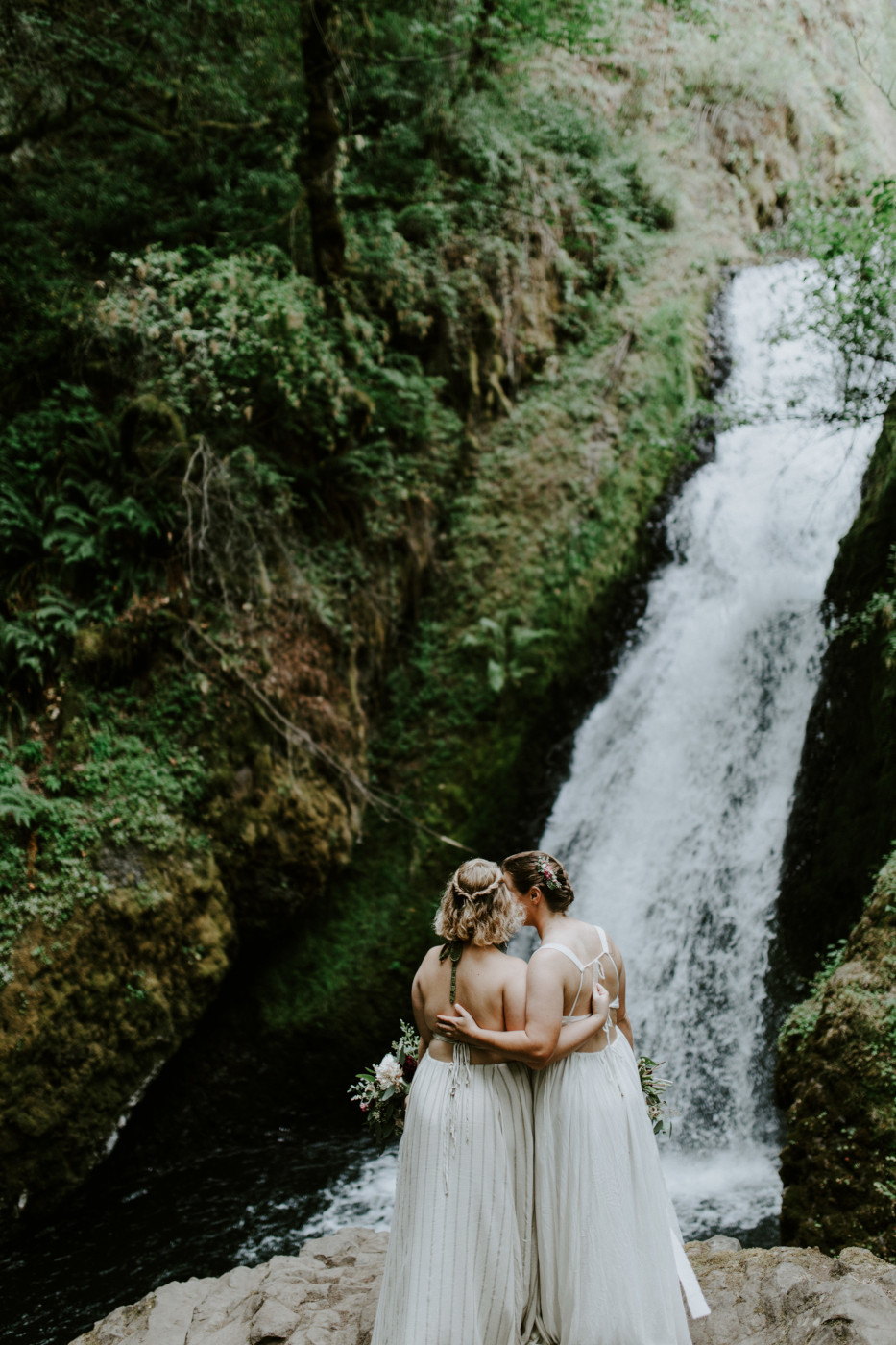 Audrey and Kate stand side by side in front of Bridal Veil Falls. Elopement wedding photography at Bridal Veil Falls by Sienna Plus Josh.