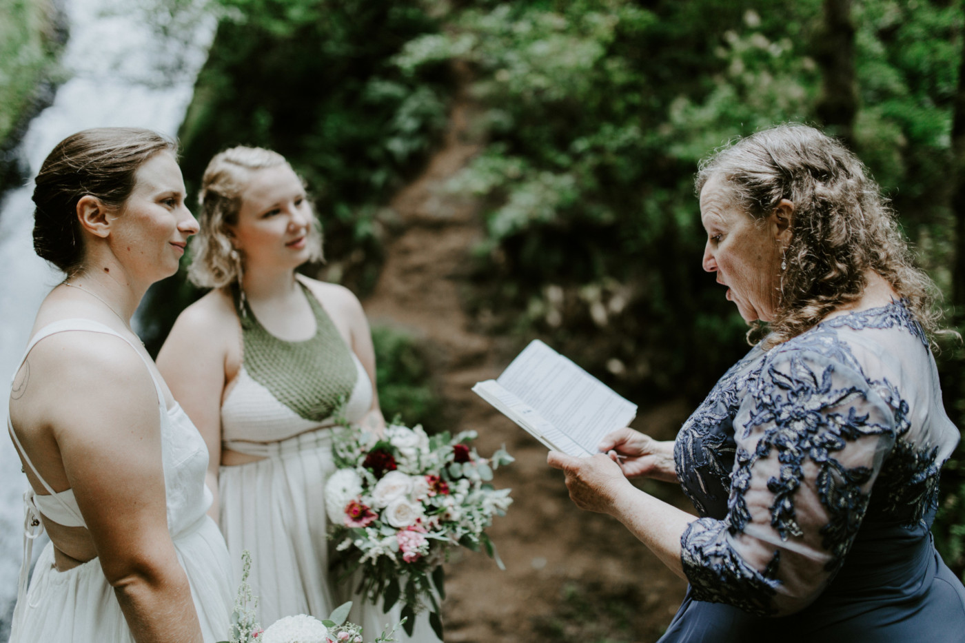 Audrey and Kate stand in front of Kate's mom as she officiates at Bridal Veil Falls. Elopement wedding photography at Bridal Veil Falls by Sienna Plus Josh.