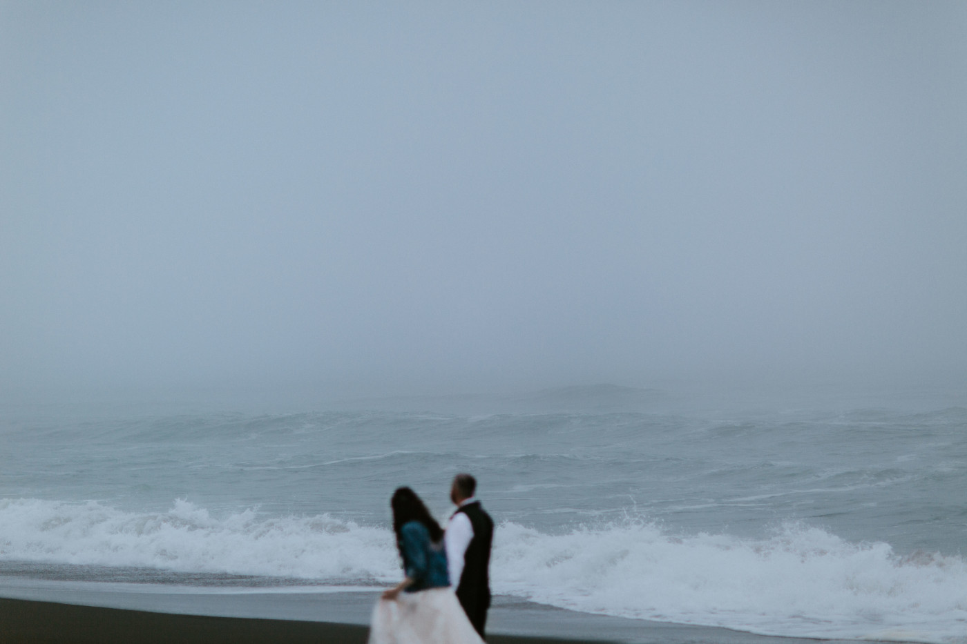 Tim and Hannah walk on the beach in front of the ocean.