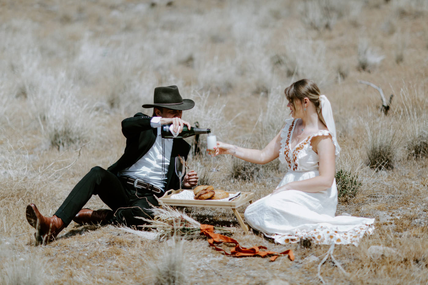 Greyson and Emily pour champagne. Elopement photography in the Central Oregon desert by Sienna Plus Josh.