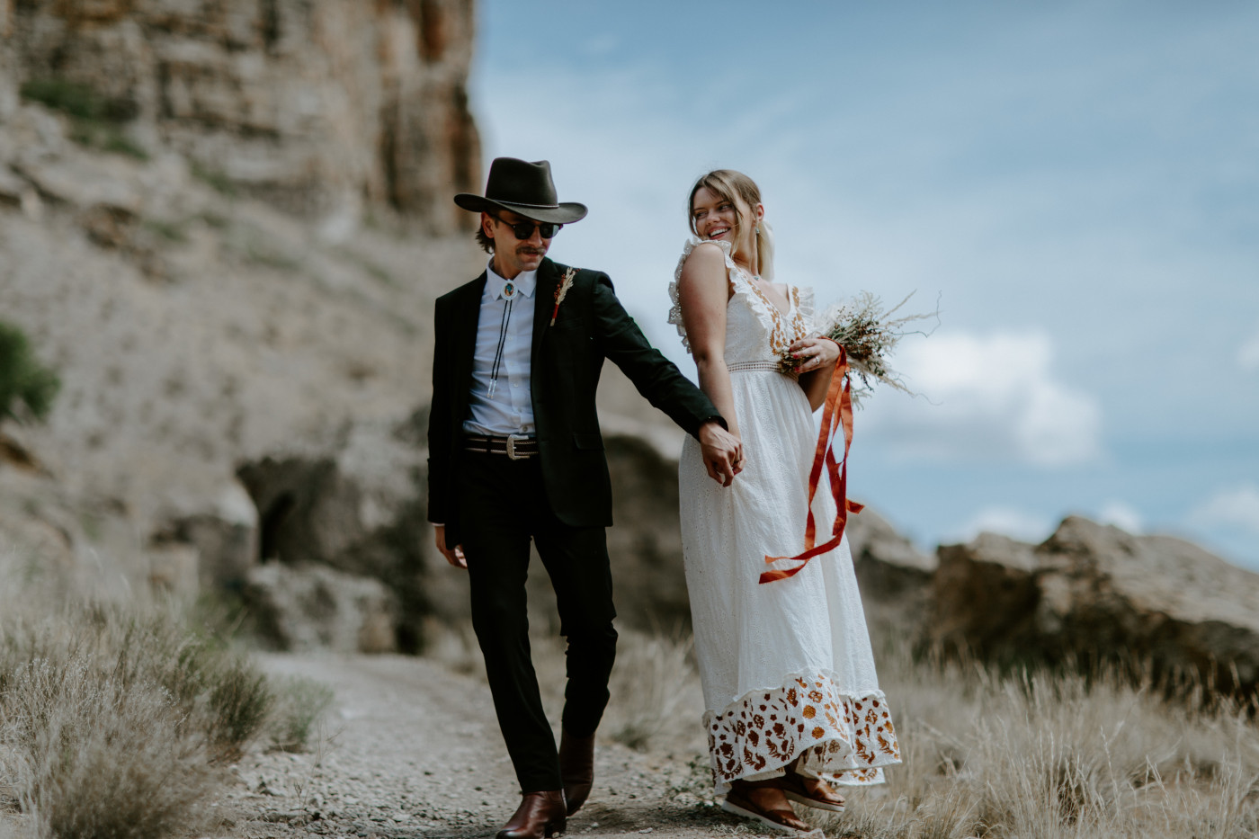 Emily and Greyson hold hands as they walk along a trail. Elopement photography in the Central Oregon desert by Sienna Plus Josh.
