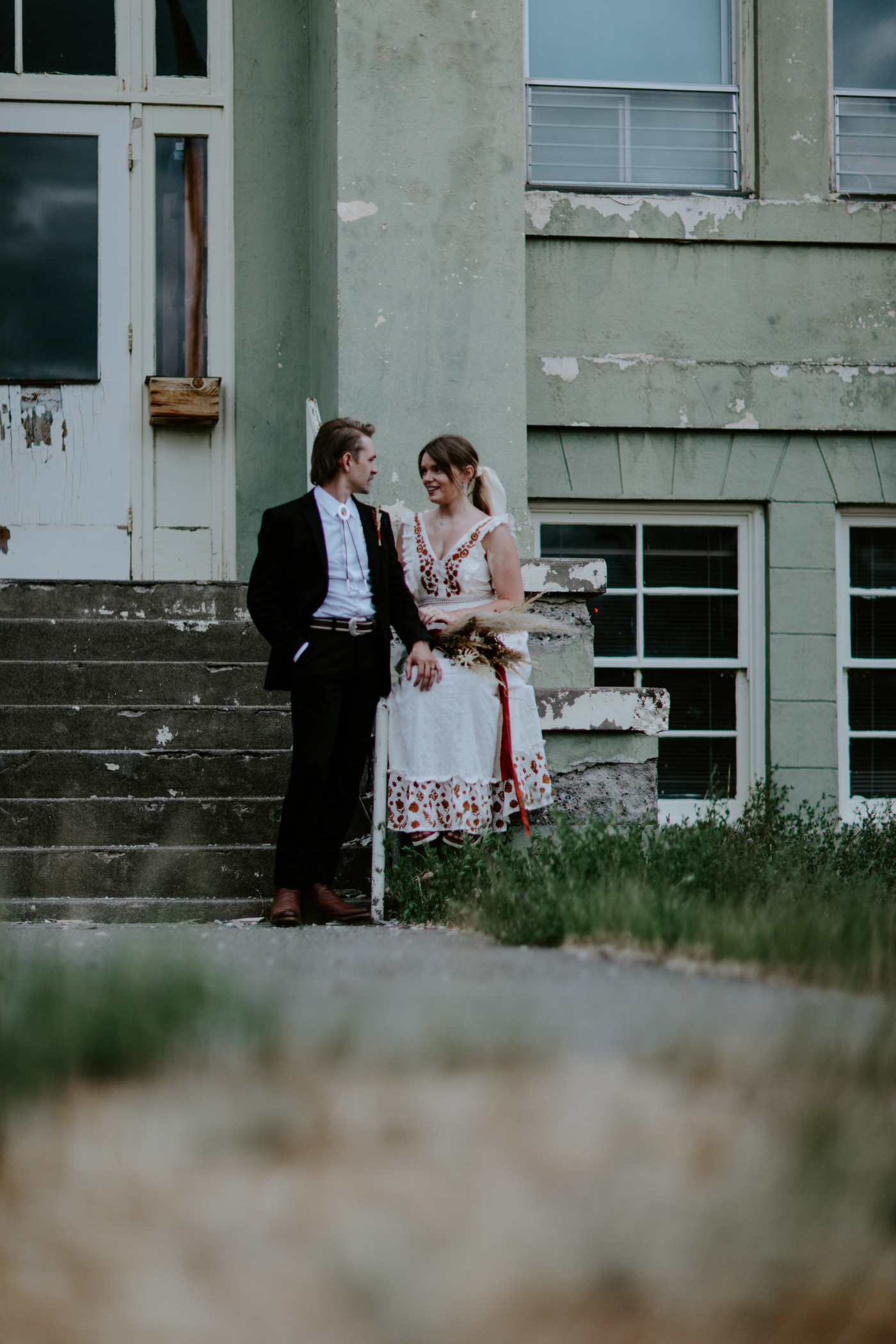 Greyson and Emily in front of an old school house. Elopement photography in the Central Oregon desert by Sienna Plus Josh.