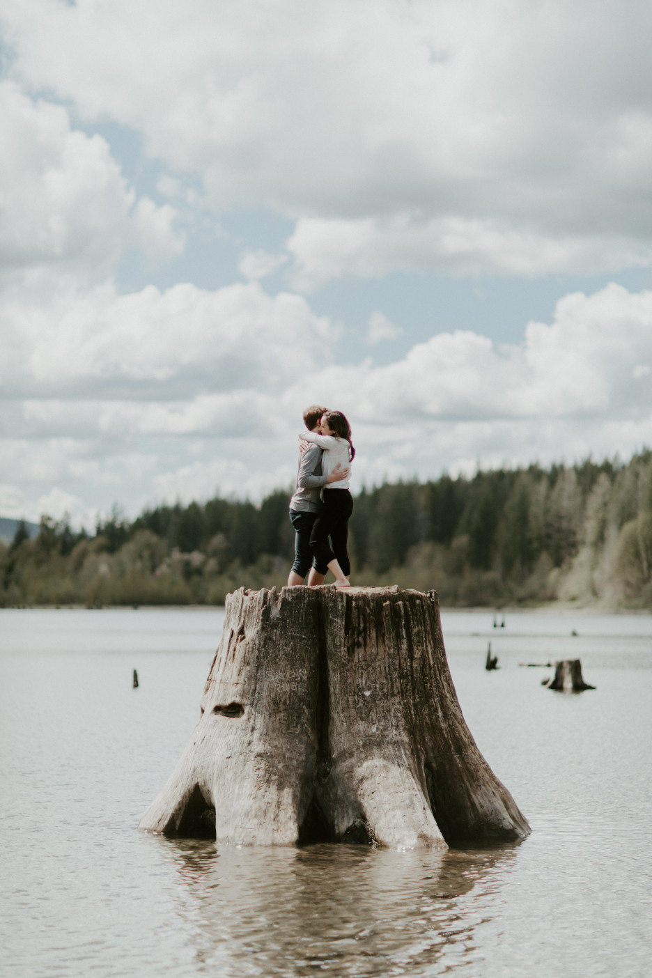 Janelle and Adam hug on top of a stump at Rattlesnake Lake, WA. Adventure engagement session at Rattlesnake Lake, Washington by Sienna Plus Josh.