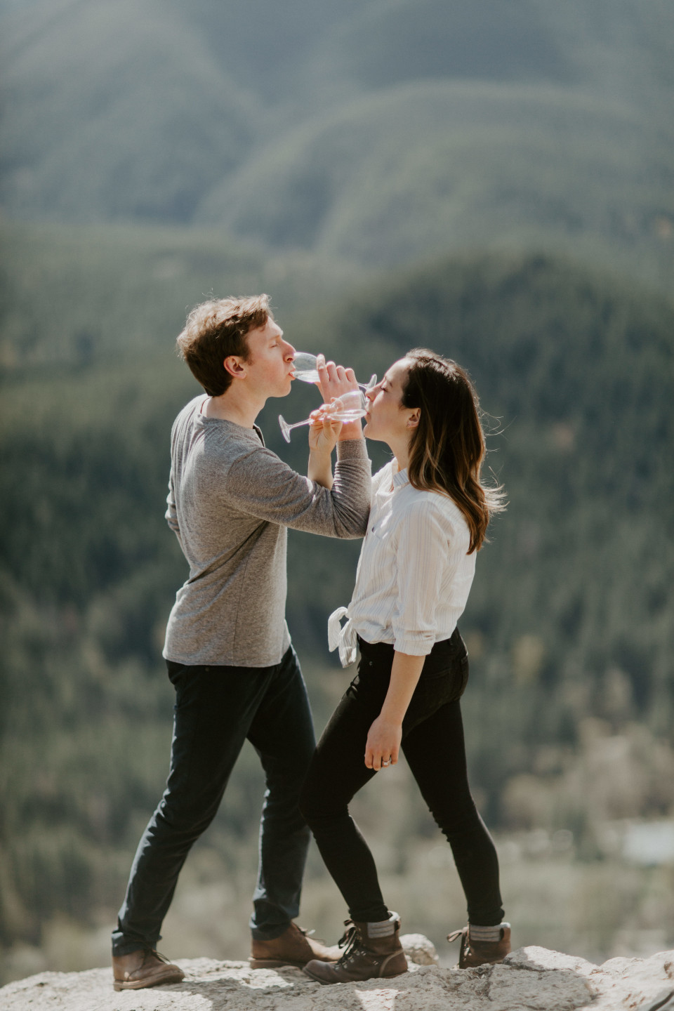 Adam and Janelle cross arms to drink champagne atop Rattlesnake Ledge. Adventure engagement session at Rattlesnake Lake, Washington by Sienna Plus Josh.