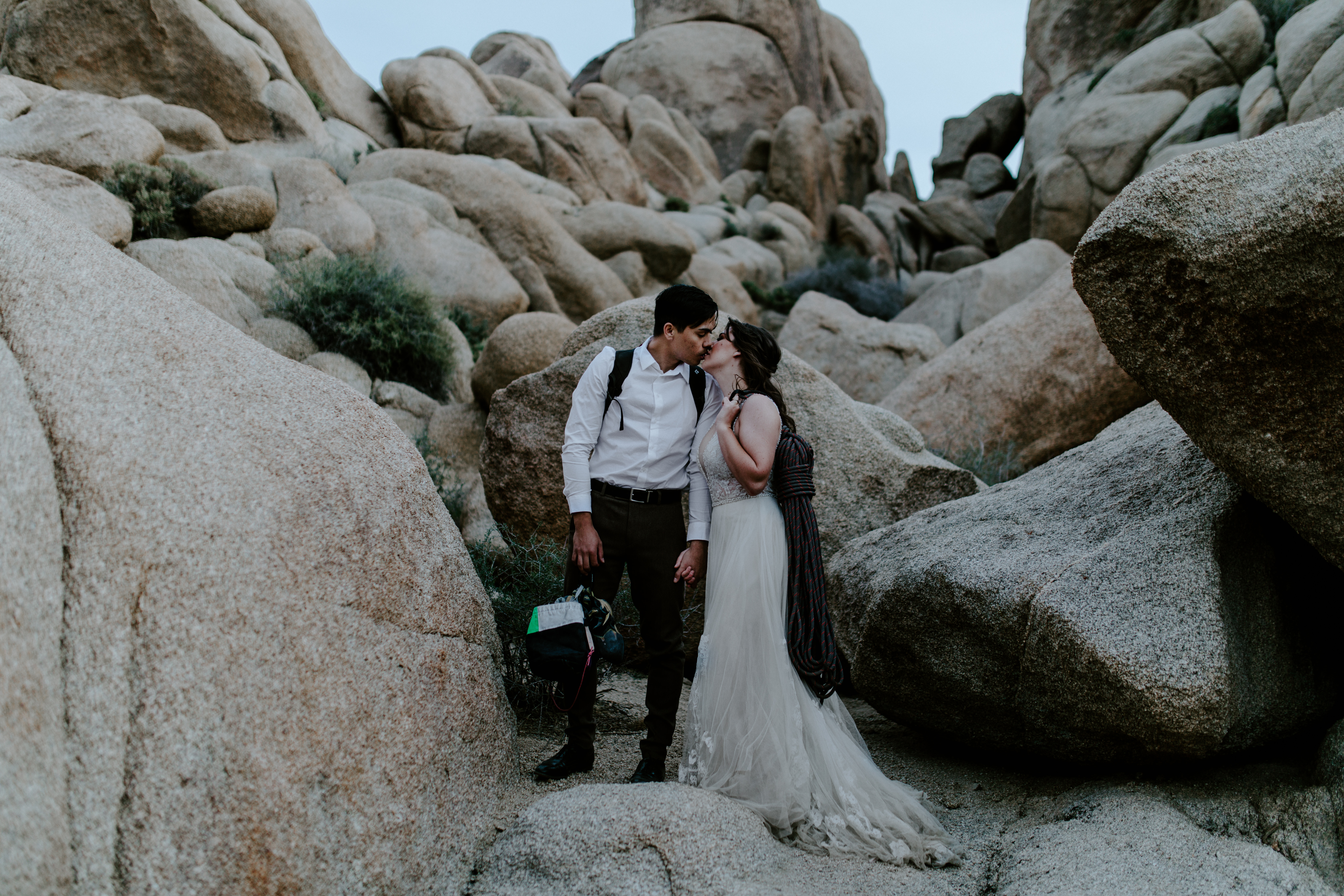 A bride and groom stand together with their gear during a hike in Joshua Tree National Park.