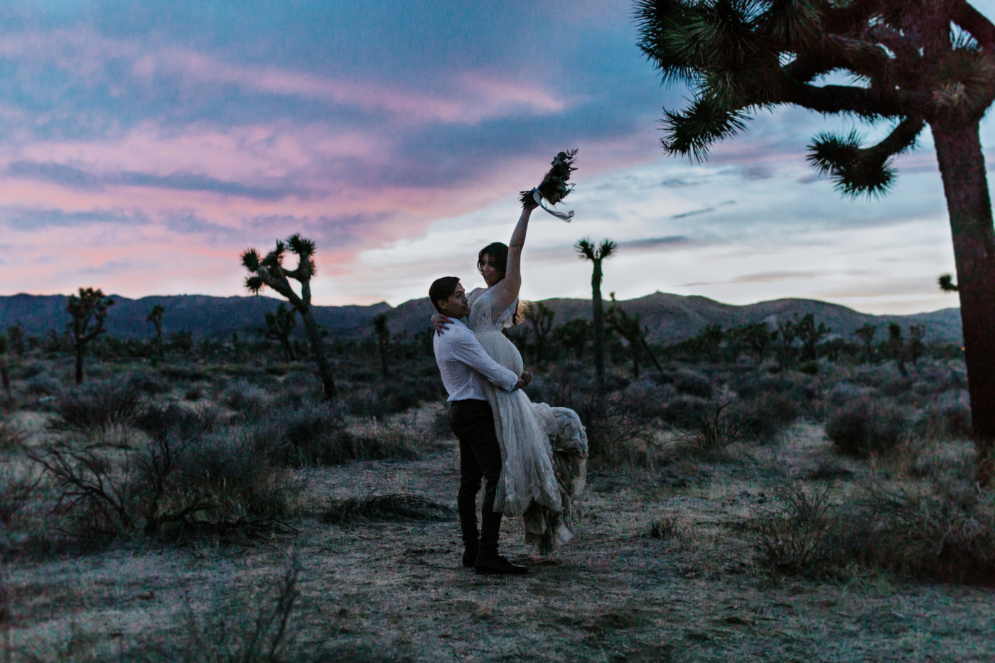 Zack picks up Shelby as she holds her flowers in the air during sunset at Joshua Tree.