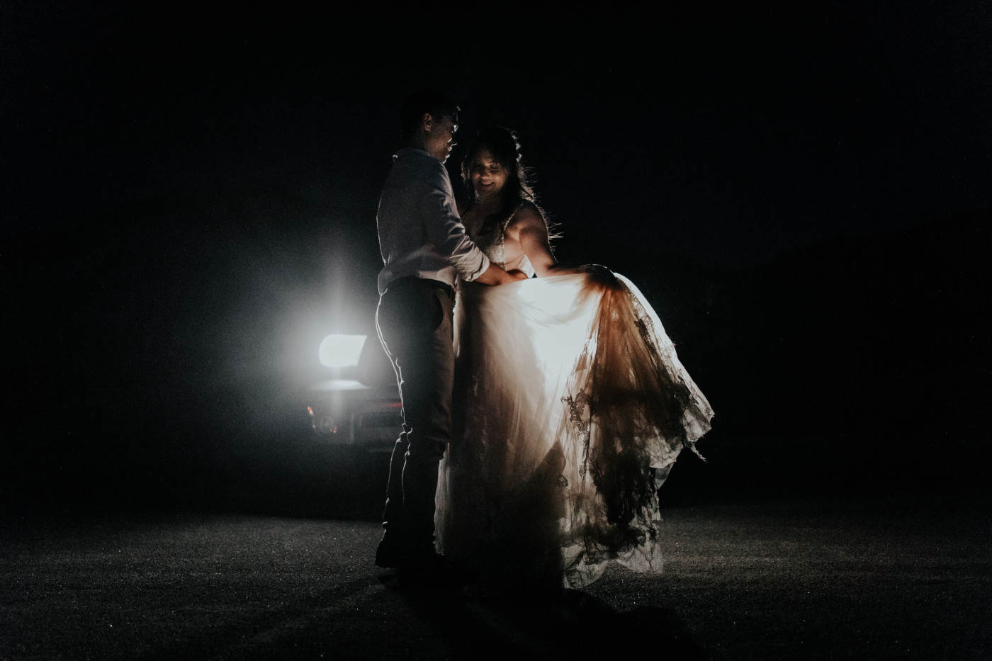 Zack holds Shelby as she holds her dress in front of their car headlights in Joshua Tree.