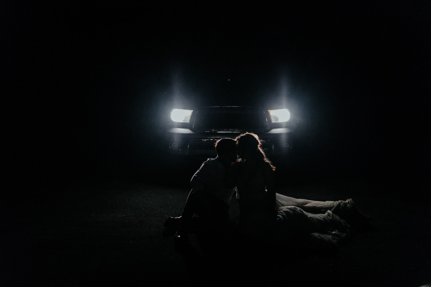 Zack and Shelby sit in front of the car headlights in the dark of Joshua Tree.