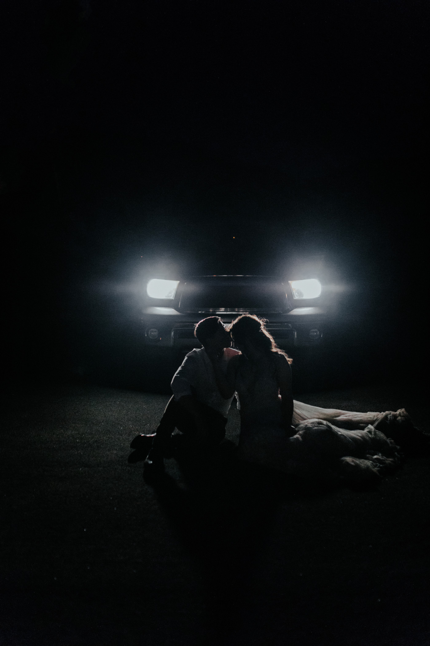 Zack and Shelby kiss in the dark while sitting in front of headlights in Joshua Tree.