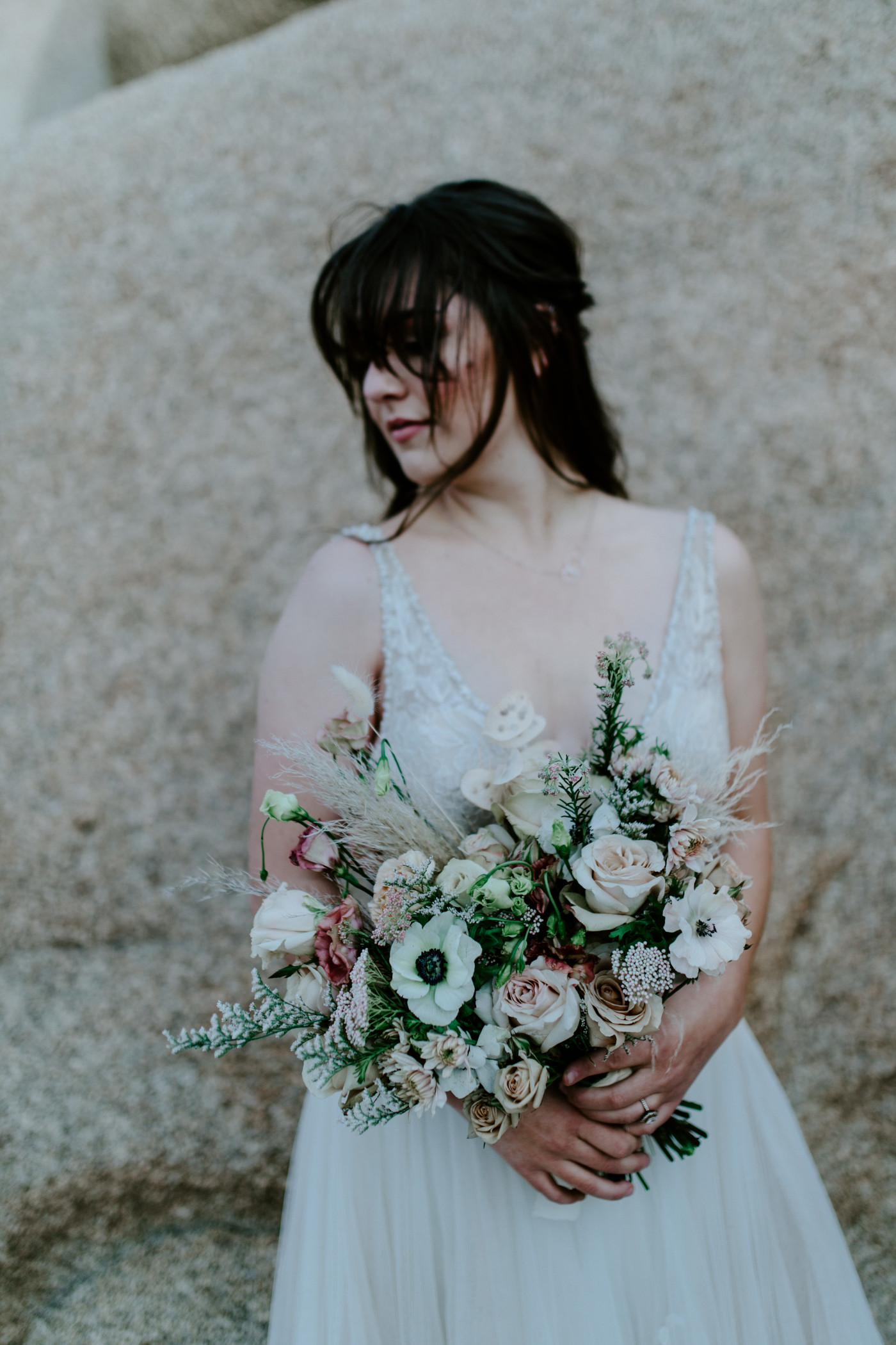 Shelby stands up against a rock in Joshua Tree with her flowers before the elopement ceremony.