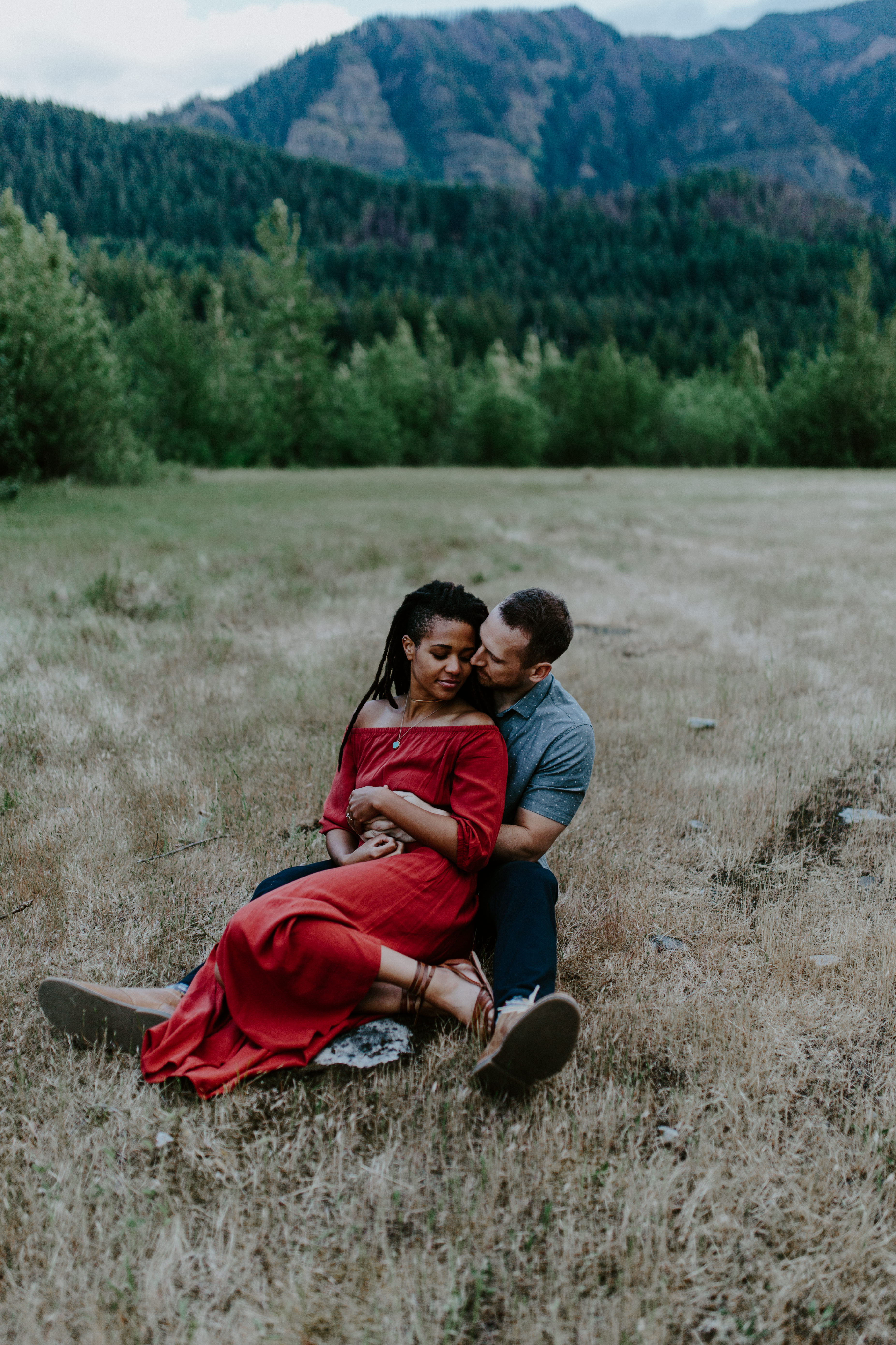 Garrett holds Kayloni as they sit in the grass during their engagement shoot at Cascade Locks in Oregon. Engagement photography in Portland Oregon by Sienna Plus Josh.