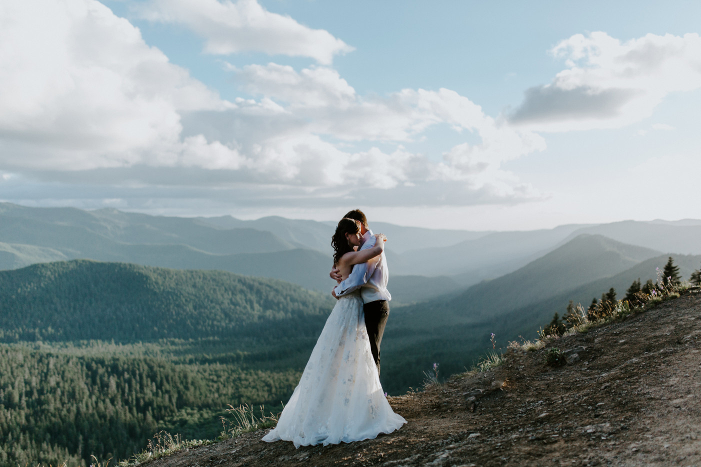 Moira and Ryan stand near a cliff with the view of the mountains in the background. Adventure elopement wedding shoot by Sienna Plus Josh.