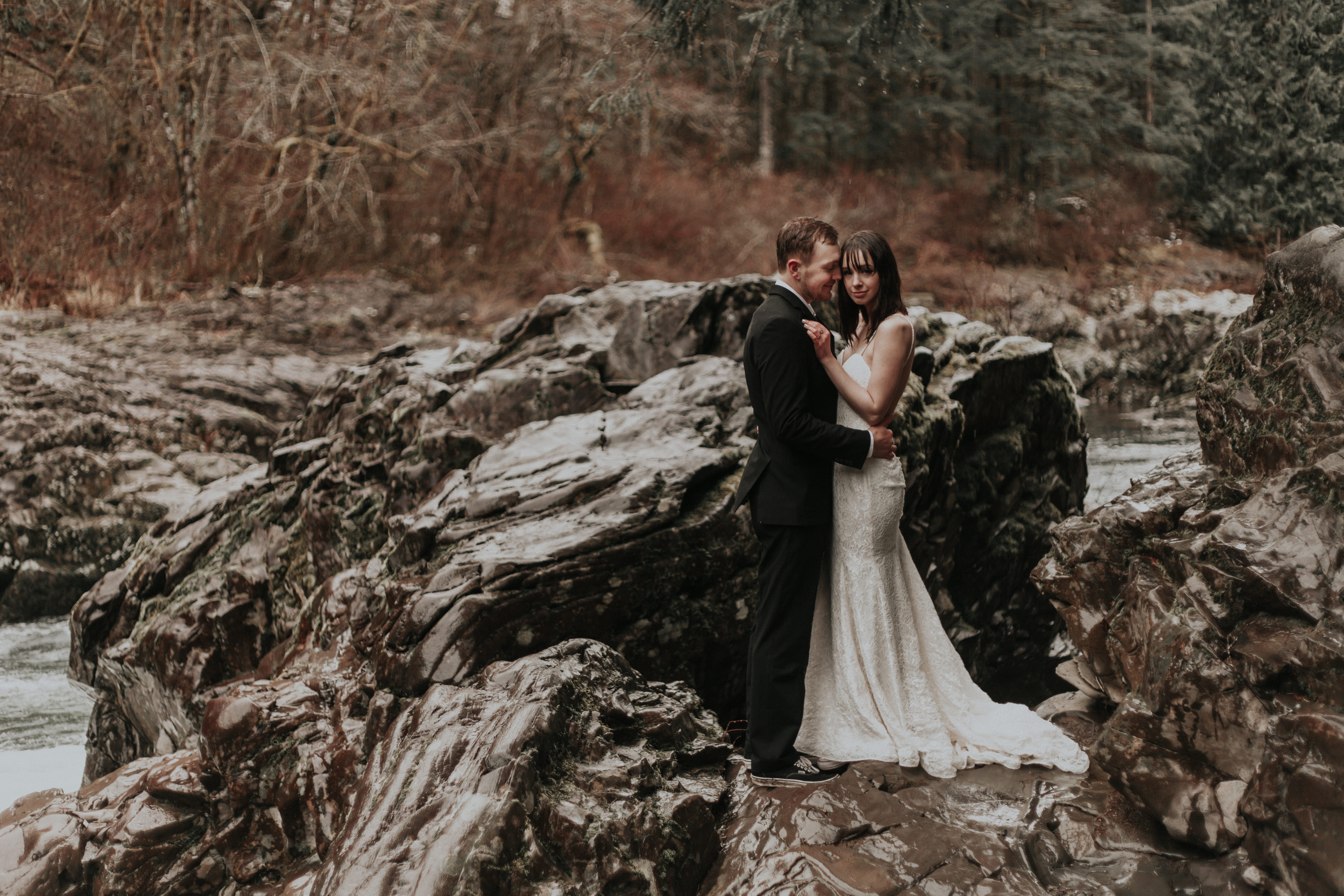Paige and TJ standing on the rocks of the river in Moulton Falls for their adventure elopement in Washington.