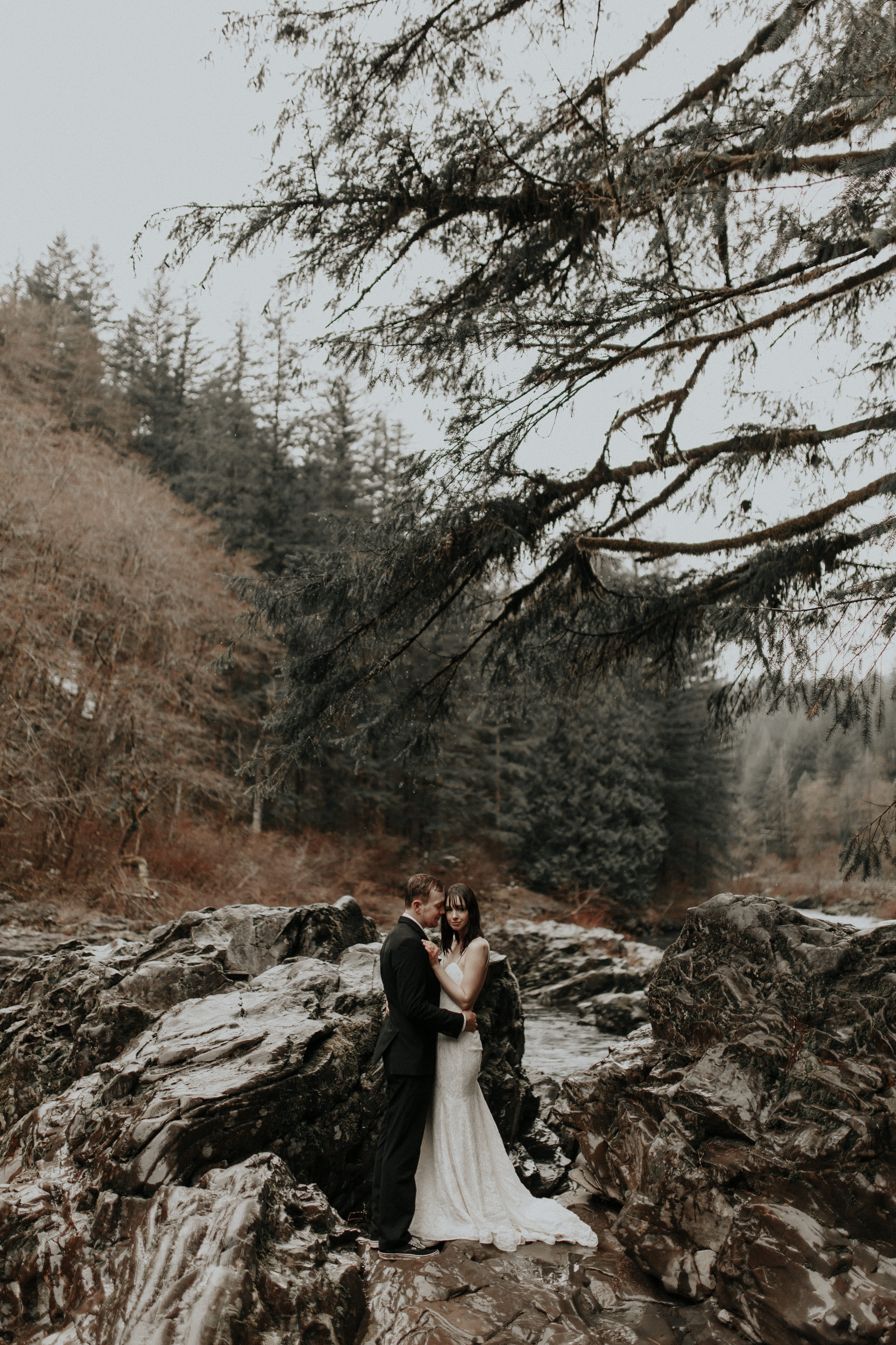 TJ and Paige standing on the boulders on the river of Moulton Falls for their adventure elopement wedding in Washington.