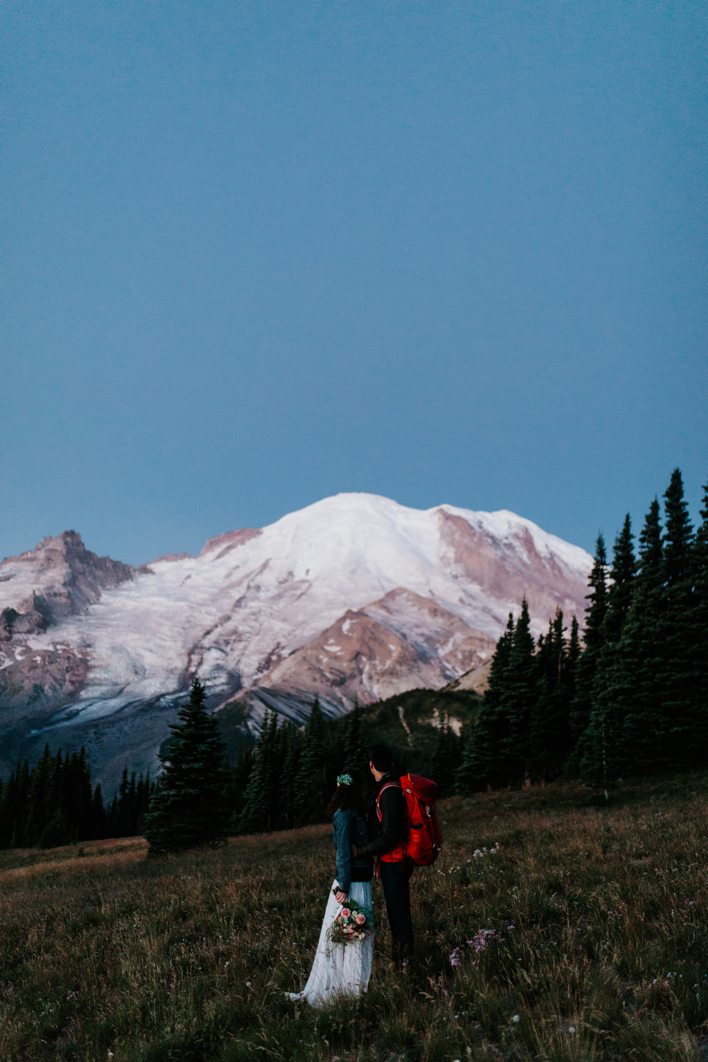 Tasha and Chad look up at the mountain from a field. Elopement photography at Mount Rainier by Sienna Plus Josh.