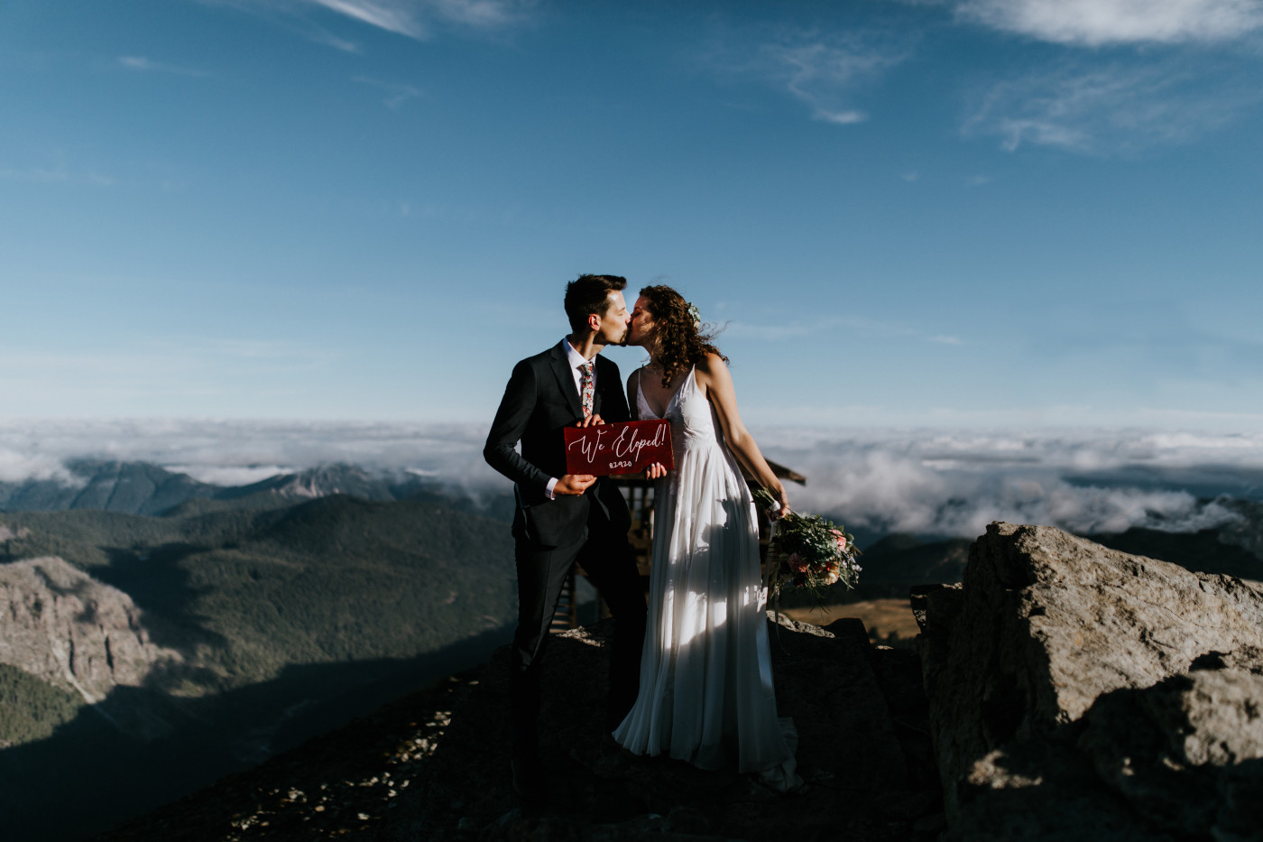Tasha and Chad kiss while holding their sign. Elopement photography at Mount Rainier by Sienna Plus Josh.