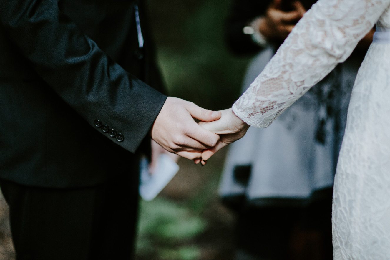 Nicole and Vlad hold hands before the ring exchange. Elopement wedding photography at Cannon Beach by Sienna Plus Josh.