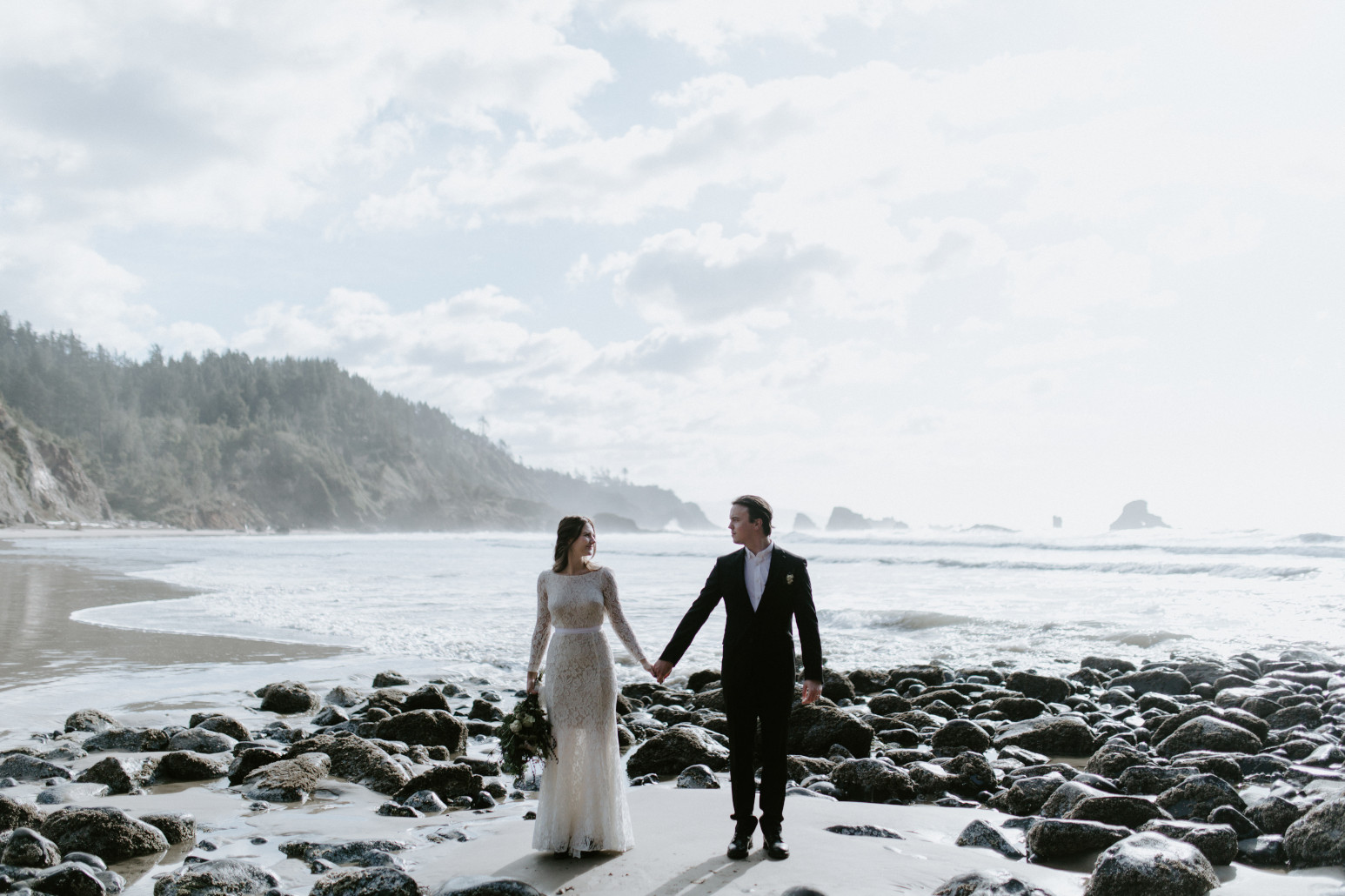 Nicole and Vlad stand next to a cliff at Indian Beach. Elopement wedding photography at Cannon Beach by Sienna Plus Josh.