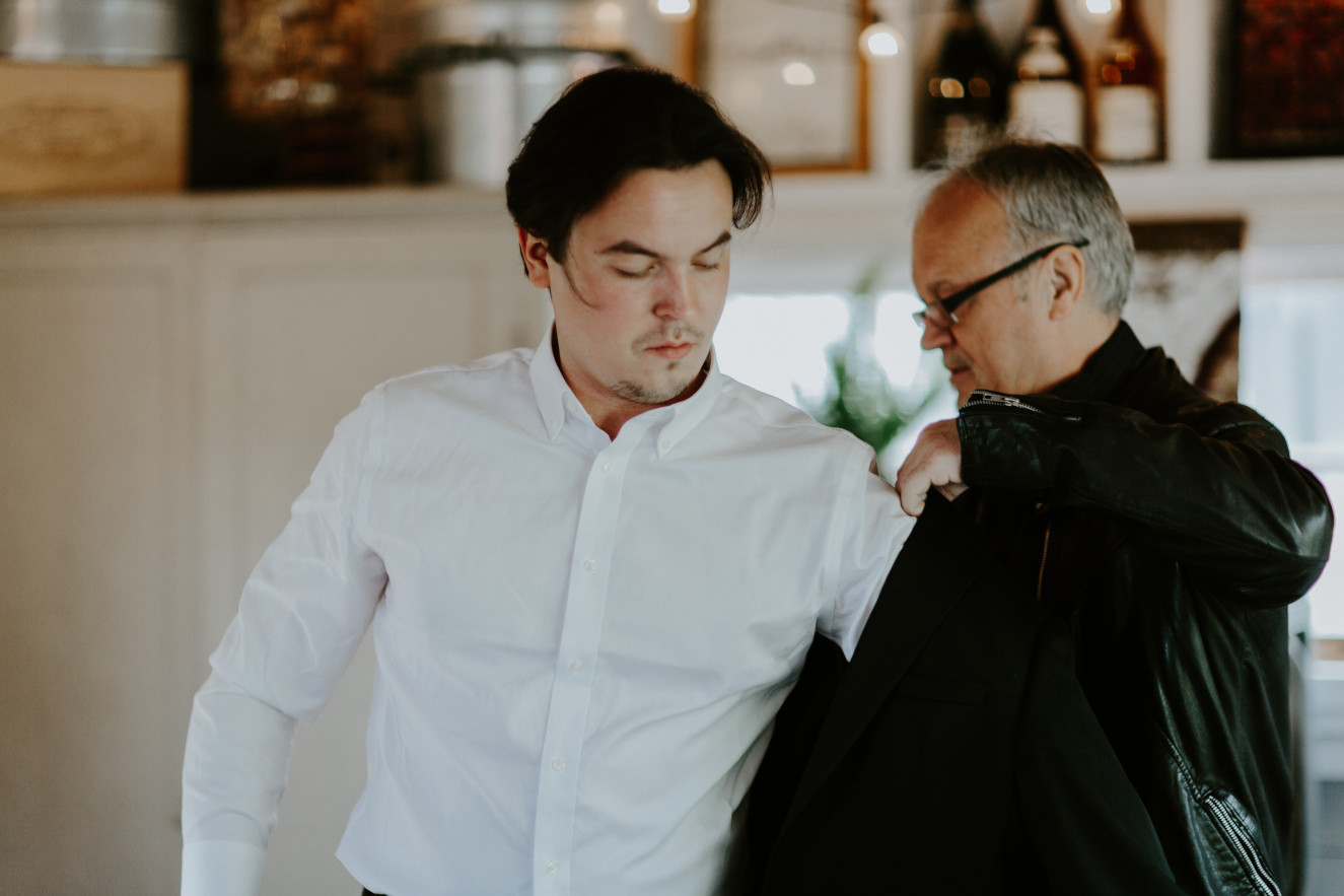 Vlad's father in law helps him put on his jacket. Elopement wedding photography at Cannon Beach by Sienna Plus Josh.