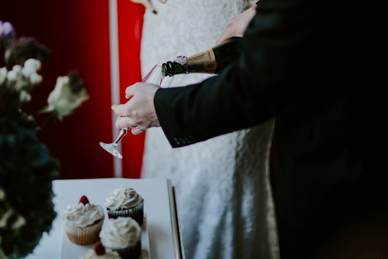 Nicole and Vlad pour a bottle of champagne. Elopement wedding photography at Cannon Beach by Sienna Plus Josh.