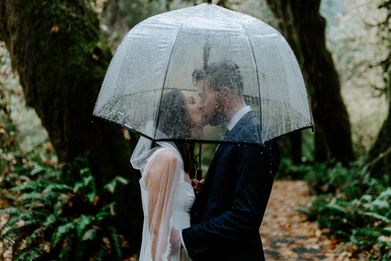Mollie and Corey kiss under the umbrella. Elopement photography in the Olympic National Park by Sienna Plus Josh.