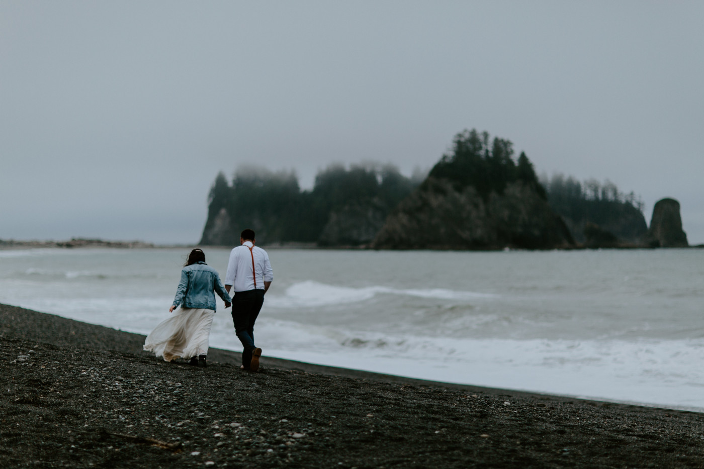 Brooke and Jack walk on the beach toward the rocks. Elopement photography at Olympic National Park by Sienna Plus Josh.