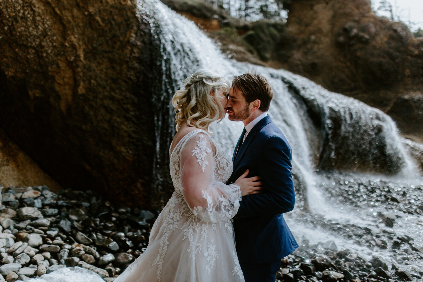 Ben and Katie go in for a kiss in front of a waterfall at the Oregon coast on the beach.