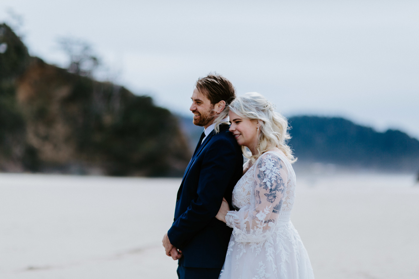 Katie and Ben stand on the sand on the beach along the Oregon coast.