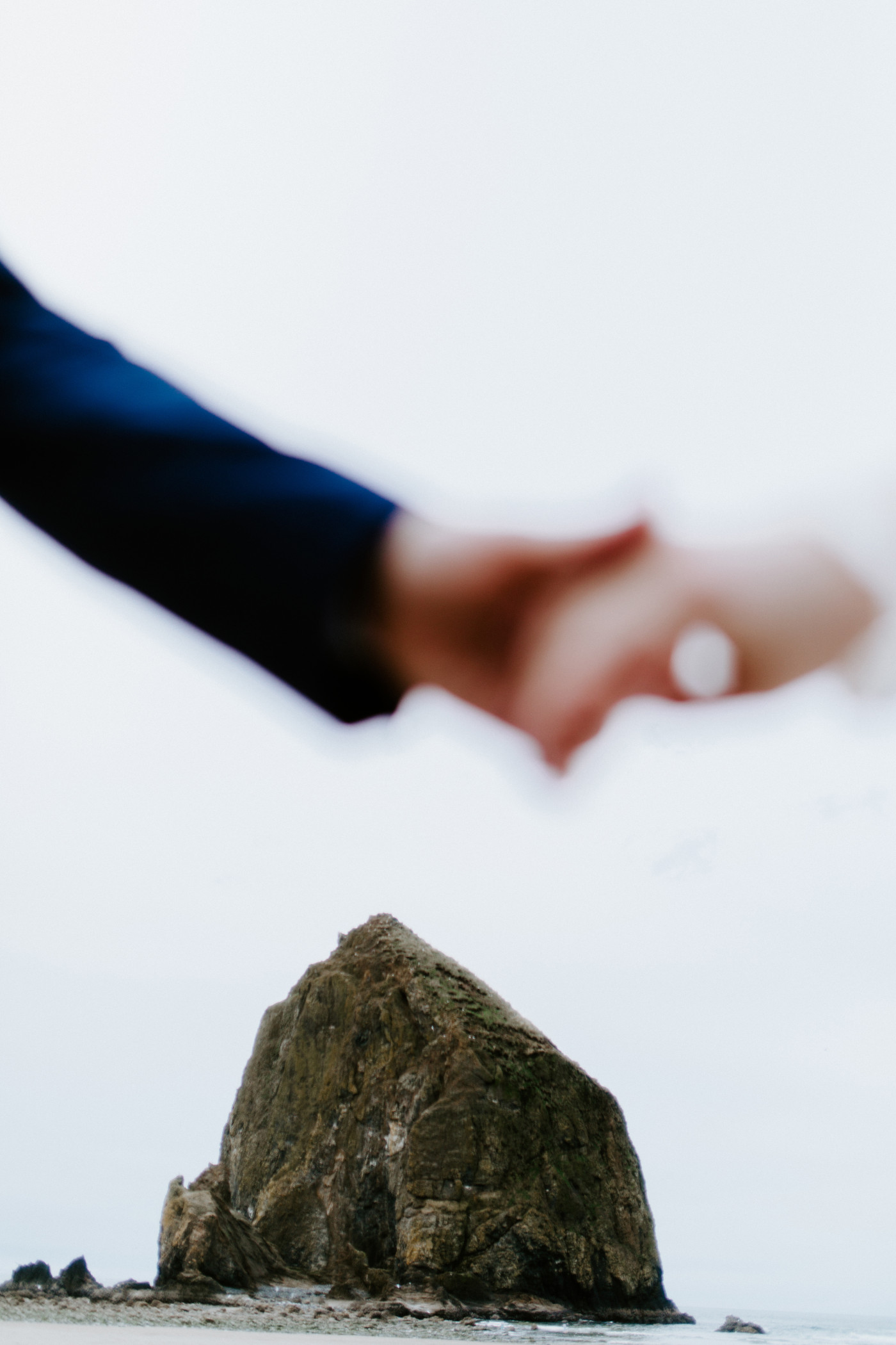 A close up of Katie and Ben holding hands on the sand on the beach along the Oregon coast.