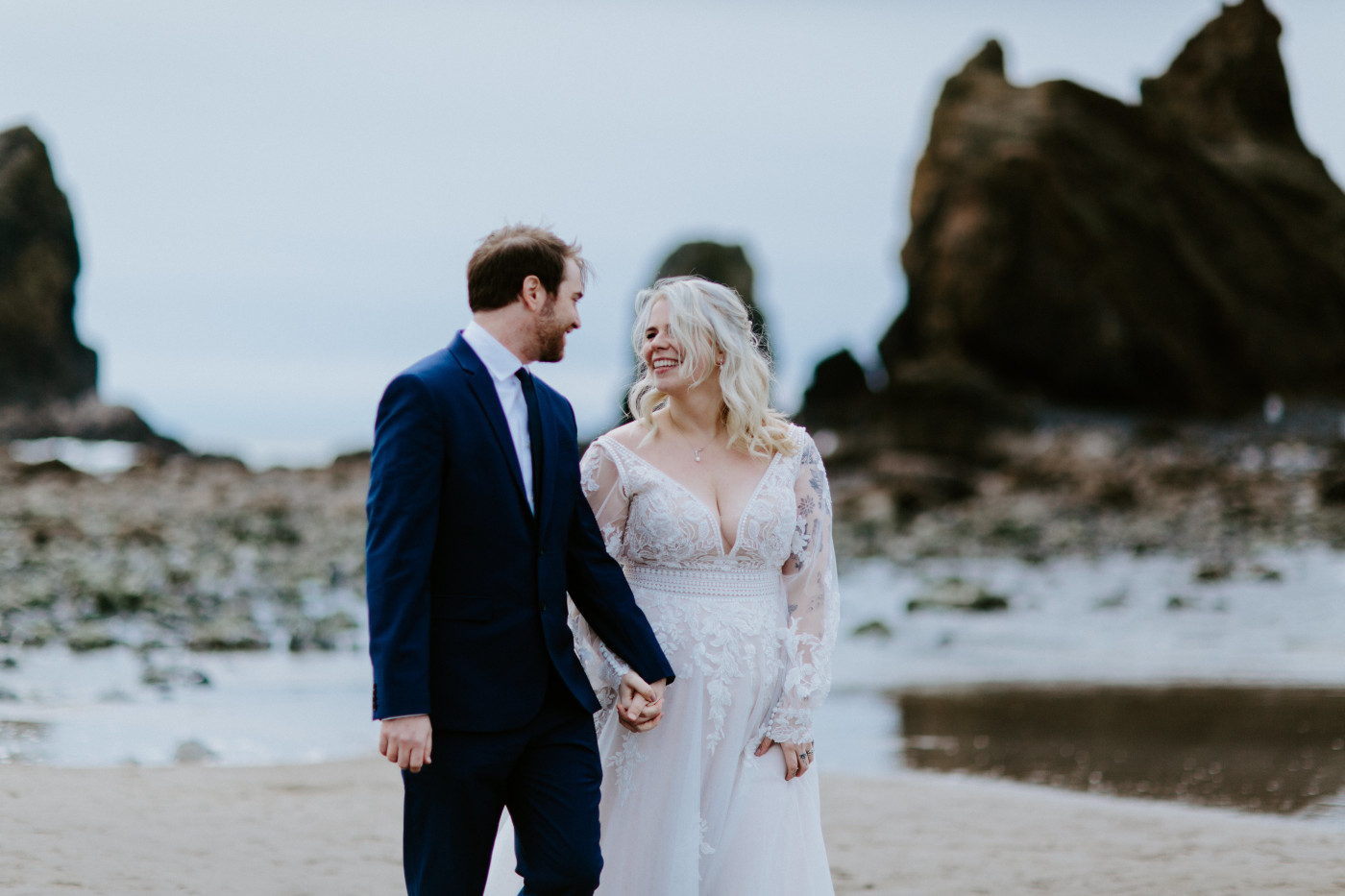 Ben and Katie smile at each other on the beach on the Oregon coast.