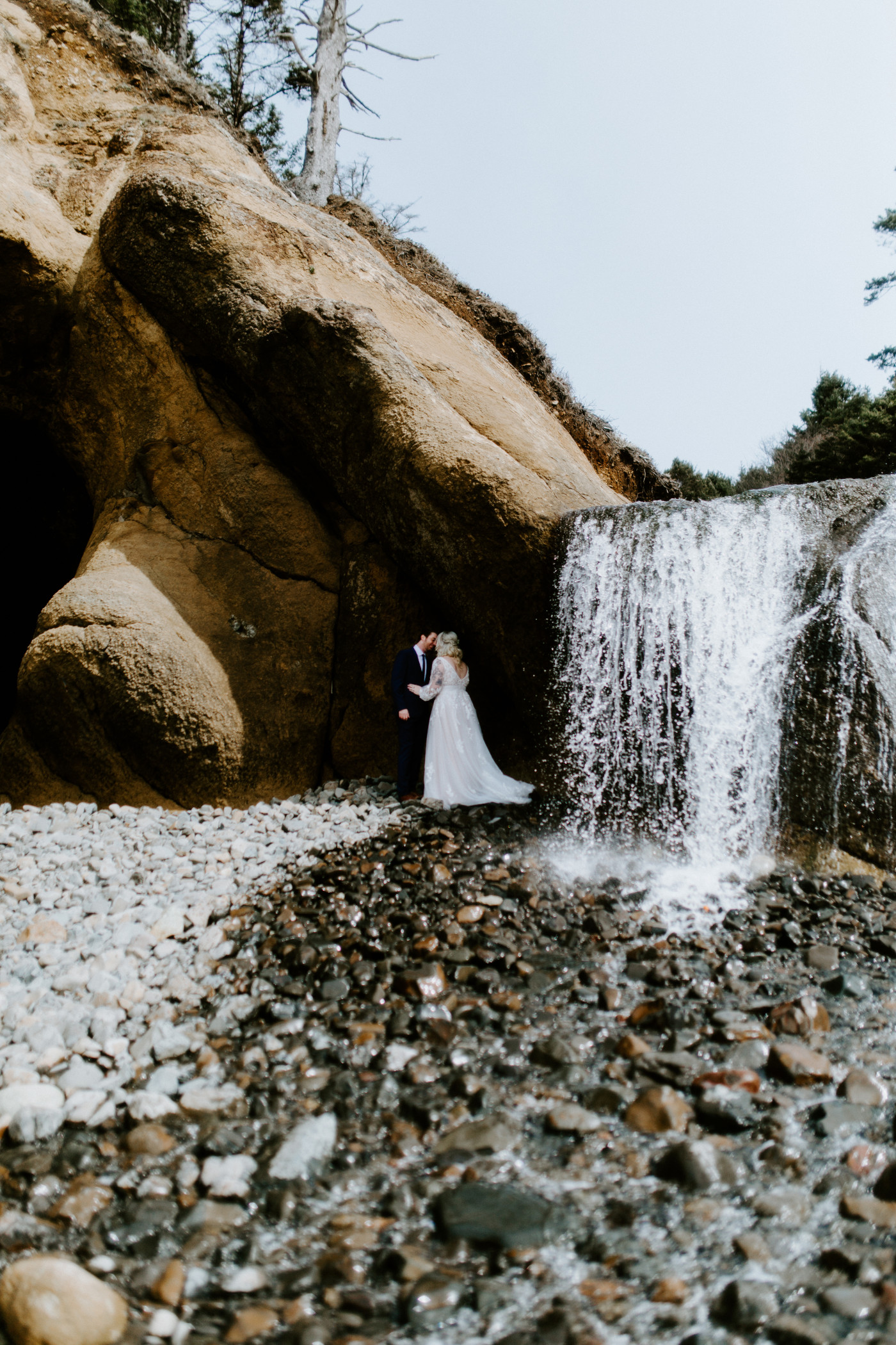 Ben and Katie stand near a waterfall at the Oregon coast on the beach.