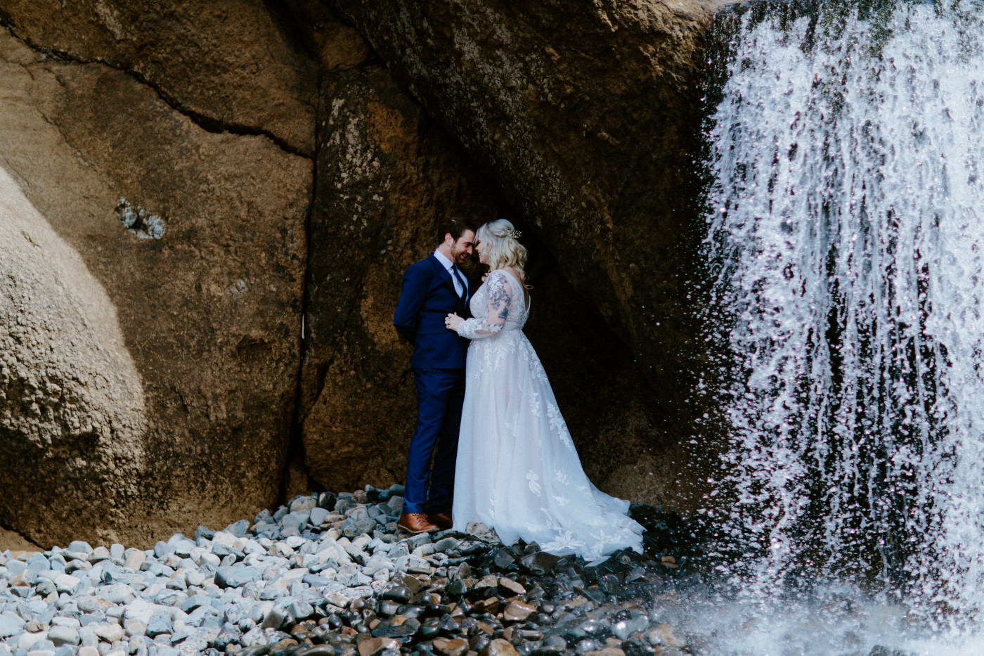 Katie and Ben stand near a waterfall at the Oregon coast on the beach.