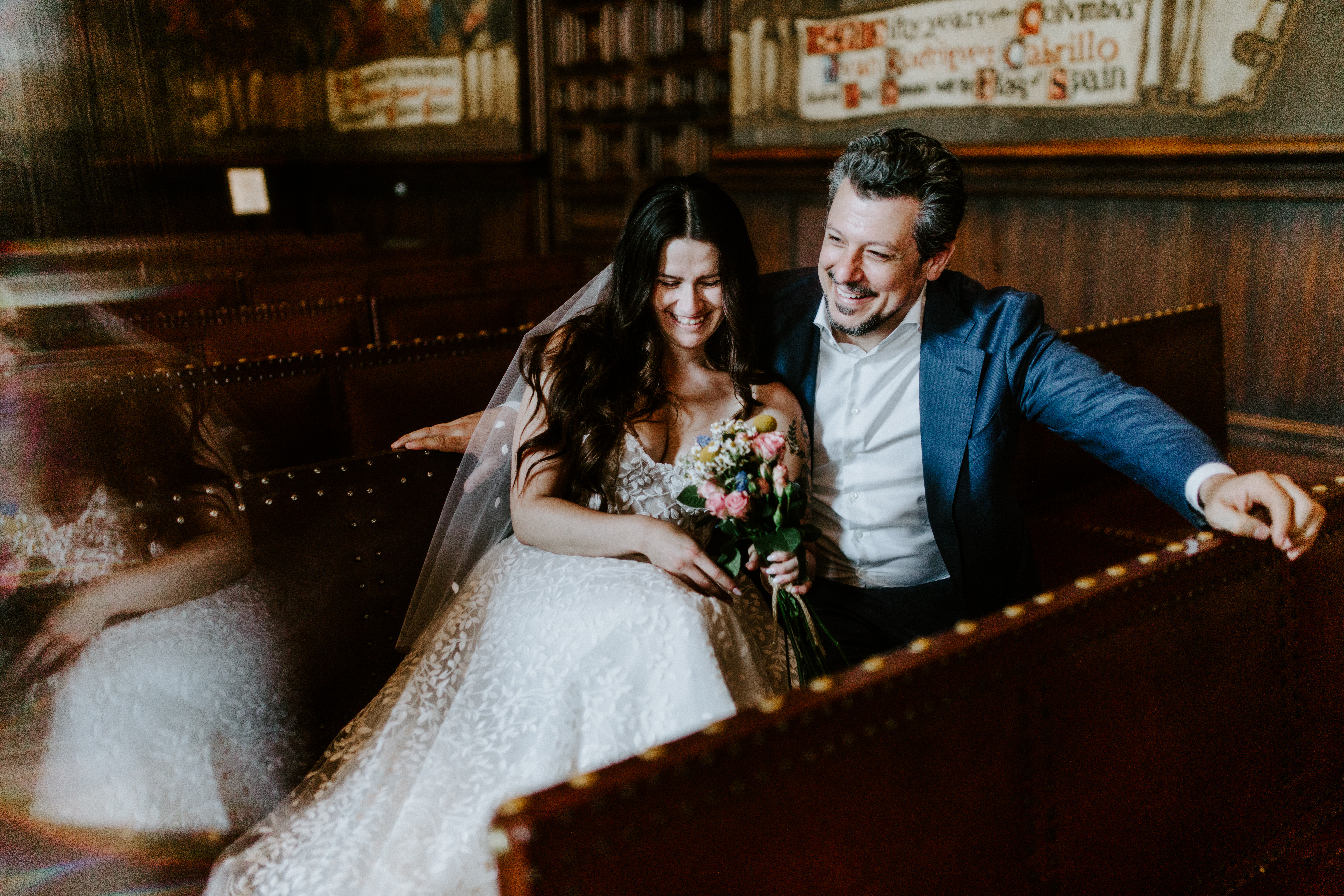 Newlyweds sit on a bench in the Mural Room in the Santa Barbara Courthouse.