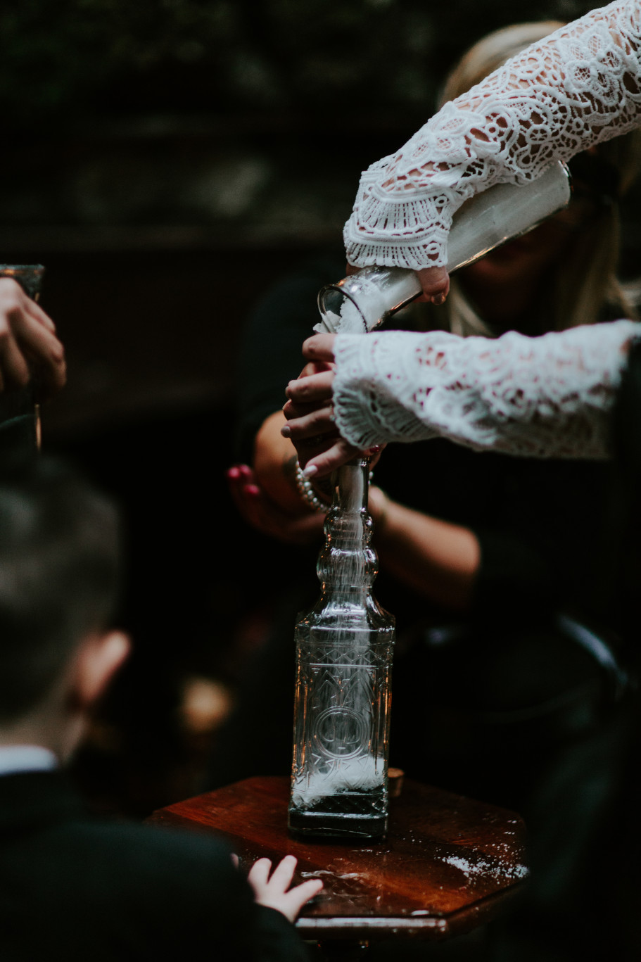 Sarah pours sand into a bottle at Skamania House, Washington. Elopement photography in Portland Oregon by Sienna Plus Josh.