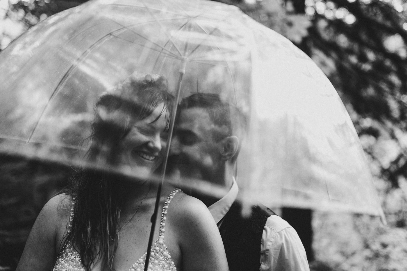 Jordan and Andrew smile while standing under an umbrella.